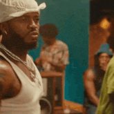 a man wearing a bandana and a white tank top is standing in a room with other men .