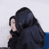 a woman with long black hair is hugging another woman with shorter black hair