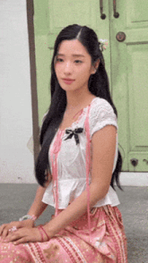 a woman in a white top and pink skirt is sitting on the ground