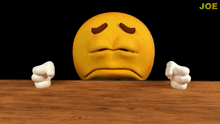 a cartoon smiley face is sitting on a wooden table with a black background and the word joe in the corner