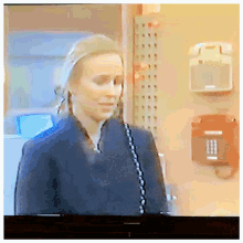 a tv screen shows a woman talking on a phone with a red box on the wall behind her
