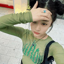 a girl wearing a green shirt with a blue ring on her finger is covering her face