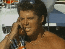 a shirtless man with a necklace is talking on a phone