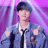 a young man wearing a denim jacket and tie gives a thumbs up