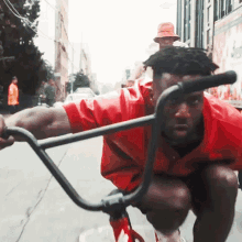 a man in a red shirt is riding a bike on the street