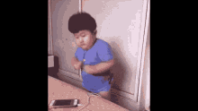 a young boy in a blue shirt is standing in front of a cell phone .