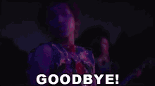 a man in a purple shirt is saying goodbye in a dark room .