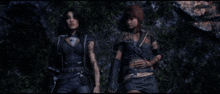 two women standing next to each other in a dark forest