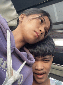 a girl wearing a purple hoodie with the letter t on it looks over a boy 's shoulder