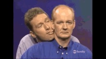 a man in a blue shirt is kissing another man on the neck .
