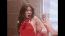 a woman in a red dress is standing in front of a mirror and making a funny face .