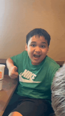 a boy wearing a green nike shirt is sitting at a table .