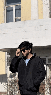 a man in a black jacket is standing in front of a building