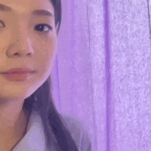 a close up of a woman 's face with a purple background and a purple curtain behind her .