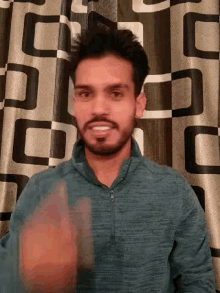 a man with a beard is laying on a bed with a checkered curtain behind him