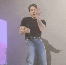 a man wearing a black shirt and blue jeans is holding a microphone