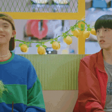 a man in a red jacket is sitting next to another man in a blue and green shirt
