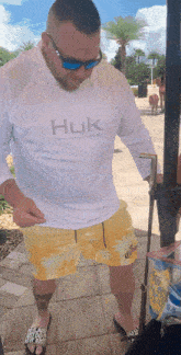 a man wearing a huk shirt and yellow shorts is standing on a sidewalk