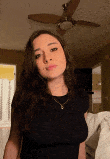 a woman in a black shirt is standing in a room with a ceiling fan in the background