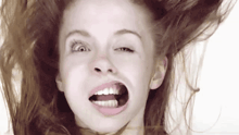 a close up of a woman making a funny face with her mouth open and her hair blowing in the wind .
