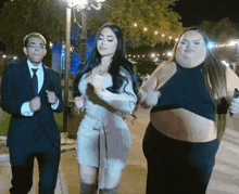 a man in a suit stands next to two women dancing