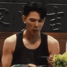 a man in a tank top is eating food with a fork .