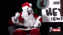 a man dressed as santa claus is sitting in front of an aew sign