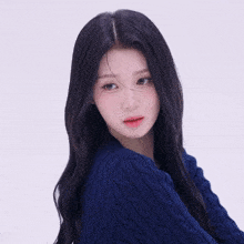 a woman with long black hair wearing a blue sweater looks at the camera