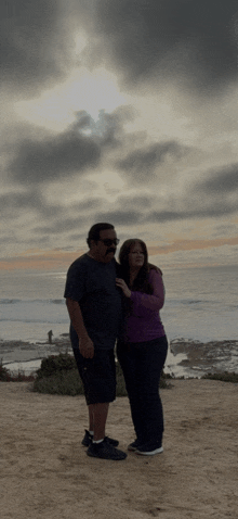 a man and a woman are posing for a picture in front of a cloudy sky