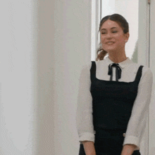 a woman in a black dress and white shirt is smiling while standing in front of a door .