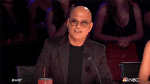 a bald man in a suit and glasses is sitting in front of a microphone with a drink in his hand .
