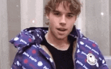 a young man is wearing a purple jacket and looking at the camera .