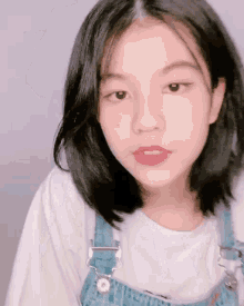 a young girl is wearing overalls and a white shirt .