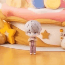 a doll is standing in front of a cake on a wooden floor .