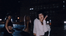 a woman in a white shirt is dancing in front of a group of women in black crop tops .