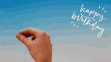 a hand writes happy birthday on a blue and white background