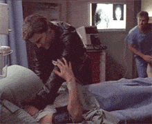 a man in a black leather jacket takes a man 's blood pressure in a hospital room