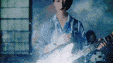 a woman in a blue shirt is playing a guitar with a band in the background