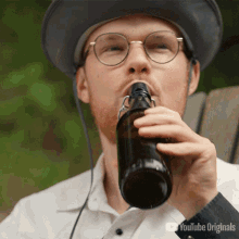 a man wearing glasses and a hat drinking from a bottle with youtube originals written on the bottom