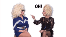 two drag queens are sitting next to each other and one of them is pointing at the other with the word oh behind her
