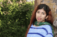 a woman leaning against a tree wearing a blue and green striped shirt