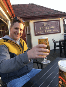 a man holds up a glass of beer in front of a sign that says the lakeside inn