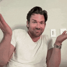 a man in a white t-shirt is making a funny face with his hands in the air .