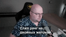 a man wearing glasses and a blue shirt is sitting in front of a microphone with a foreign language caption