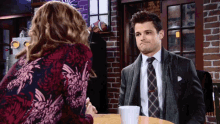a man in a suit and tie is sitting at a table talking to a woman