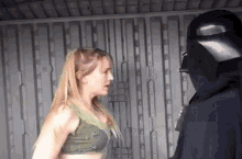 a woman in a green tank top is standing next to a man in a black helmet .