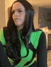 a woman with long black hair is wearing a green top and black pants