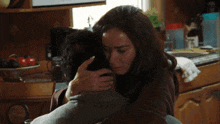 a woman is hugging a man in a kitchen with a bowl of tomatoes in the background