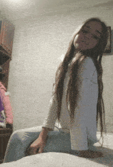 a girl with long hair is sitting on a bed with her hands on her knees