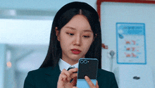 a woman in a suit is holding a cell phone in her hand .